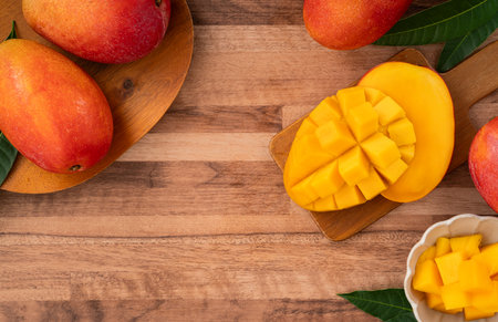 Juicy yellow mango cubes with whole mangoes on a wooden table backgroundの写真素材