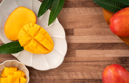 Juicy yellow mango cubes with whole mangoes on a wooden table backgroundの写真素材