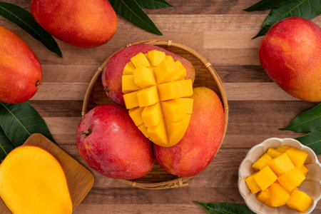Juicy yellow mango cubes with whole mangoes on a wooden table backgroundの写真素材