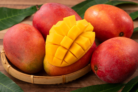 Juicy yellow mango cubes with whole mangoes on a wooden table background.の写真素材