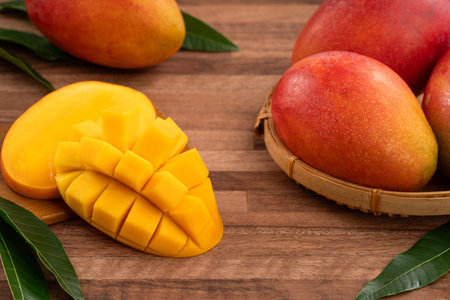 Juicy yellow mango cubes with whole mangoes on a wooden table background.の写真素材