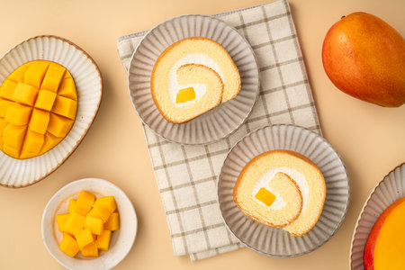 Delicious mango cream Swiss roll cake served on a plate with fresh mango cubes.の写真素材