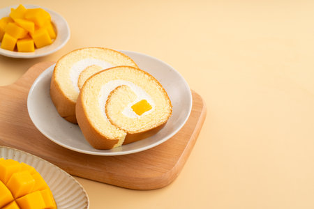 Delicious mango cream Swiss roll cake served on a plate with fresh mango cubes.の写真素材