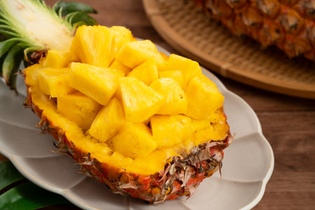 Juicy pineapple chunks arranged in a halved pineapple bowl with tropical leaves in the background.の写真素材