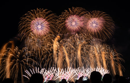 Brilliant fireworks burst above a crowd during a dazzling nighttime celebration near a bridge in...