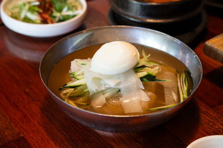 Refreshing Korean cold noodles served in chilled broth with sliced vegetables and boiled egg.の写真素材