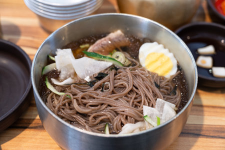 Refreshing Korean cold noodles served in chilled broth with sliced vegetables and boiled egg.の写真素材