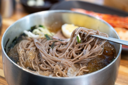 Refreshing Korean cold noodles served in chilled broth with sliced vegetables and boiled egg.の写真素材