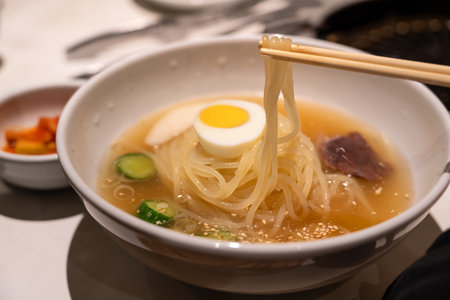 Refreshing Korean cold noodles served in chilled broth with sliced vegetables and boiled egg.の写真素材