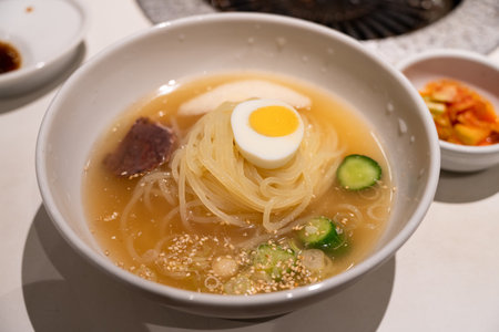 Refreshing Korean cold noodles served in chilled broth with sliced vegetables and boiled egg.の写真素材