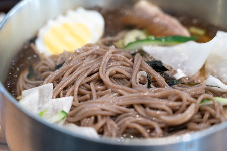 Refreshing Korean cold noodles served in chilled broth with sliced vegetables and boiled egg.の写真素材