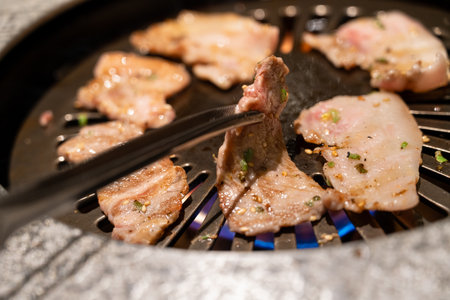 Marinated pork belly slices being grilled in BBQ restaurant.の写真素材