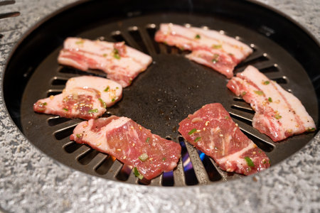 Marinated pork belly slices being grilled in BBQ restaurant.の写真素材