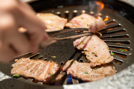 Marinated pork belly slices being grilled in BBQ restaurant.の写真素材