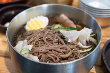 Refreshing Korean cold noodles served in chilled broth with sliced vegetables and boiled egg.の写真素材