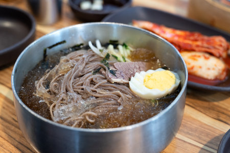 Refreshing Korean cold noodles served in chilled broth with sliced vegetables and boiled egg.の写真素材