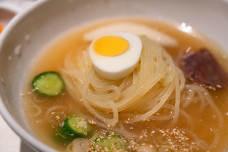 Refreshing Korean cold noodles served in chilled broth with sliced vegetables and boiled egg.の写真素材