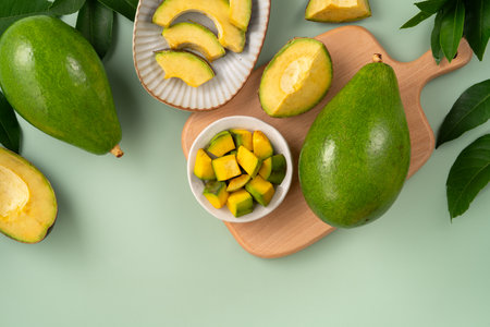 Whole and sliced avocados with diced pieces over green table background.の写真素材