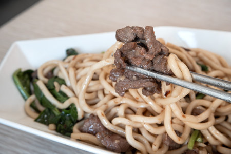 Delicious stir-fried beef noodles with green vegetables on a wooden table.の写真素材