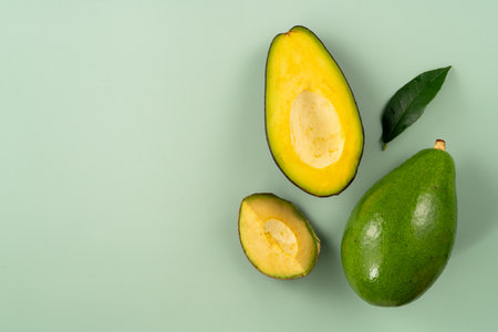 Whole and sliced avocados with diced pieces over green table background.の写真素材
