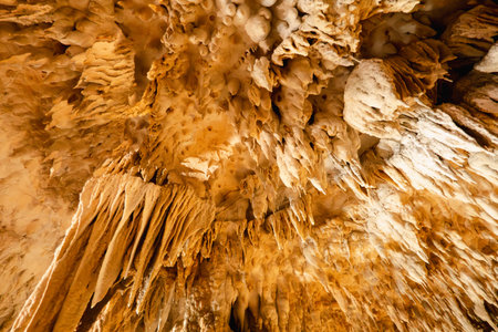 Natural stalactites and stalagmites speleothems in limestone cave with illuminated lighting.