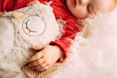 Cute little baby girl sleeping on light blanket with plush owl, little hand on fron viewの写真素材