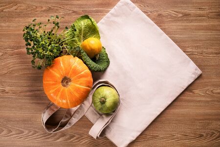 Fresh vegetables, pumpkins, cabbage leaf with green grass in pot, flatlay on eco bag and wooden background tableの写真素材