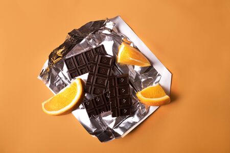 Chocolate bar broken in pieces with segments of an orange on foil insert on yellow backgroundの写真素材