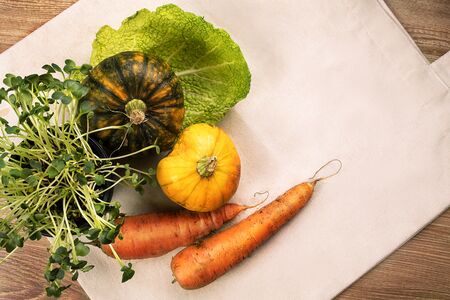 Fresh vegetables, pumpkins, cabbage leaf with green grass in pot, flatlay on eco bag and wooden background tableの写真素材