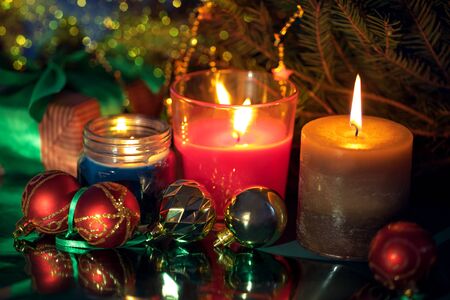 Festive christmas burning candles ubder the evegreen tree with gift box wrapped in natural paper with atlas bow and baubles aside, blur bokehの写真素材