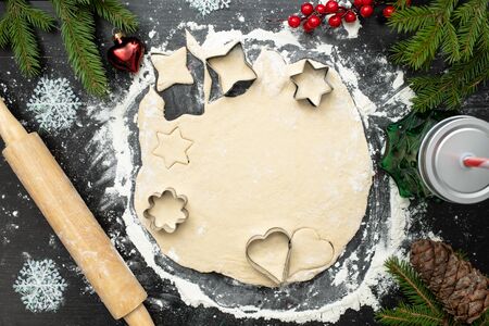 Christmas cooking, ginger cookies or biscuits , raw dough with cutters and rolling pin on dark table decorated with spruce branches and berriesの写真素材