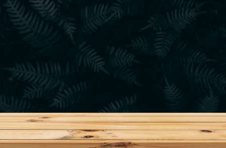 Dark leaves background with smooth wooden table product displayの写真素材