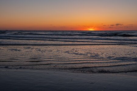 Amazing sunset view on the beach. Beautiful sunset landscape at the North sea and orange sky above it with awesome sun golden reflection on waves as a background.の写真素材
