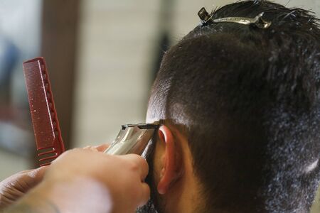 Close up shot: Barber working with hair clipper. Hipster client getting haircut. Haircut, styling...