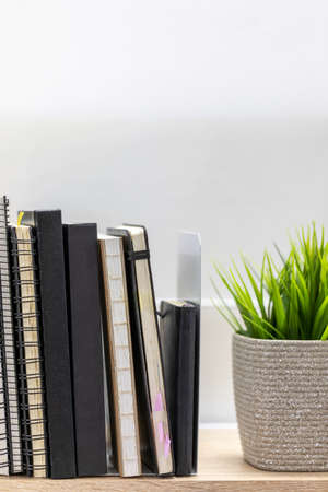 Row of sketchbooks on wooden shelf beside with house plant on white backgroundの写真素材