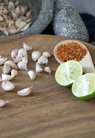 Thai cooking kitchen concept, garlics in stone mortar beside with pestle and piece of lime and dry chilly on wooden spoonの写真素材