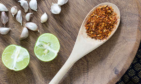 Closed up common Thai cooking ingredients concept, garlics beside with pieces of lime and dried chilly on wooden spoonの写真素材