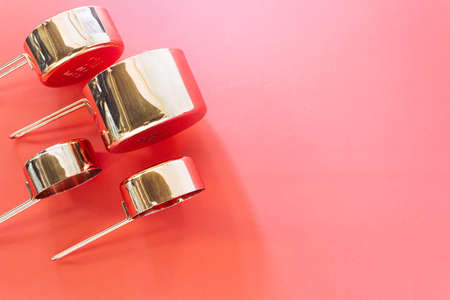 Collection of empty copper measuring cups on red background in top view