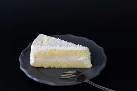 Sliced of coconut cake on dish with fork, dark moody concept, on dark background.の写真素材