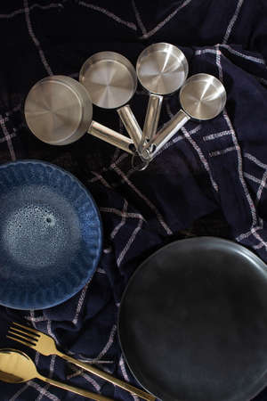 Dark kitchen concept, set of measuring spoon, empty plate and gold fork, blue textured cloth background.の写真素材