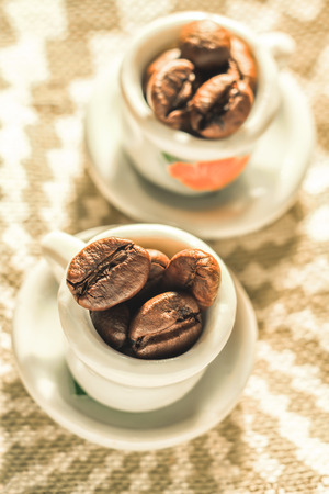 Coffee beans in a small lovely porcelain cups close-up. Strong coffee poster. Creative cozy design.の写真素材
