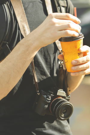 a man with a mirrorless system camera drinking coffee outdoorsの写真素材