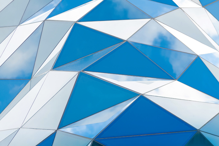 Polygonal triangle glass facade of modern building. Cloudy sky reflects in glassの写真素材