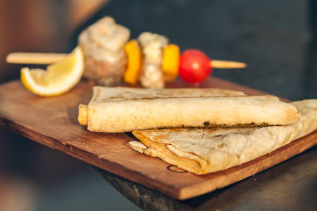 Pita bread and fish barbecue with cherry tomato and lemon on wooden cutting board.