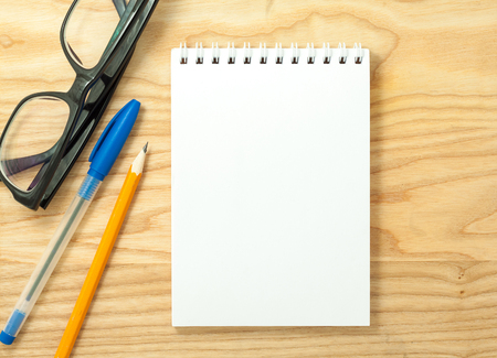 Top view of open spiral blank notebook, glasses, pen and pencil on wood desk backgroundの写真素材