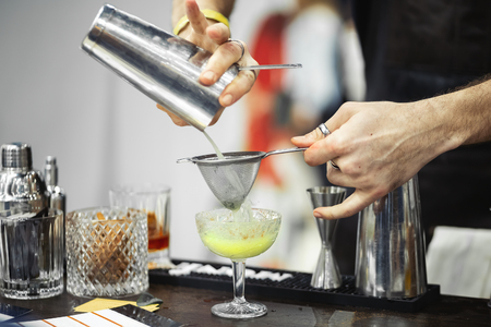 Strain through strainer. Barmen makes cocktail. Hands close-up. Strain through strainerの写真素材