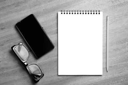 Business essentials. Top view of spiral blank notebook and smartphone on wood desk backgroundの写真素材