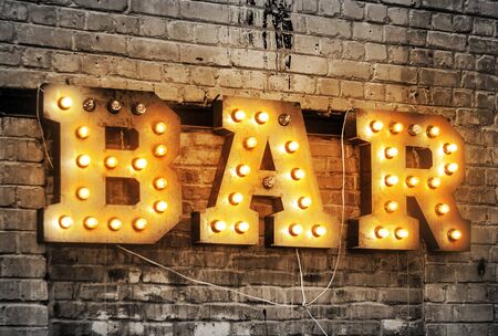 Bar signboard. Inscription from large metal letters decorated with glowing light bulbs on the brick wallの写真素材