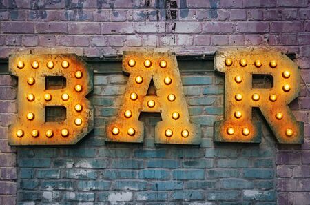 Bar signboard. Inscription from large metal letters decorated with glowing light bulbs on the brick wallの写真素材