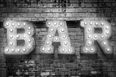 Bar signboard. Inscription from large metal letters decorated with glowing light bulbs on the brick wallの写真素材